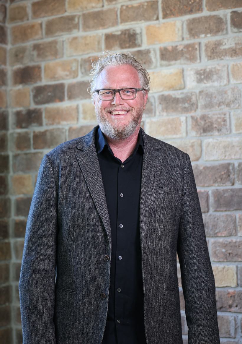 Ron Hollis in a charcoal jacket against a brick wall