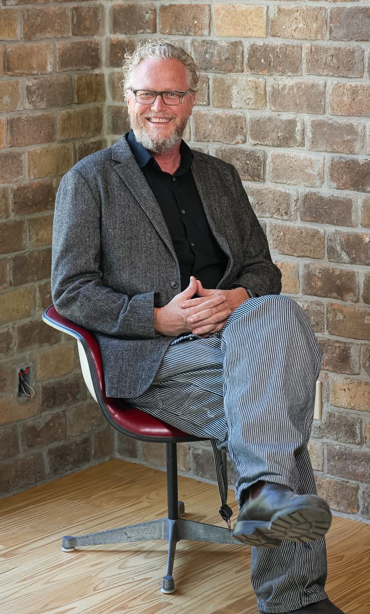 Ron Hollis seated on a red chair against a brick wall